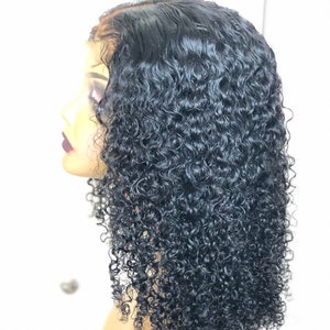 May include: A black, curly wig displayed on a mannequin head. The wig has a natural hairline and is cut to shoulder length. The tightly coiled curls have a glossy finish, giving a voluminous look. The mannequin head is a light skin tone.