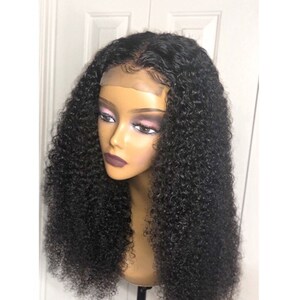 May include: A black curly wig displayed on a mannequin head. The wig has a lace front and a realistic hairline. The hair is styled in a voluminous, bouncy, curly pattern. The mannequin has a neutral skin tone and is mounted on a black stand.