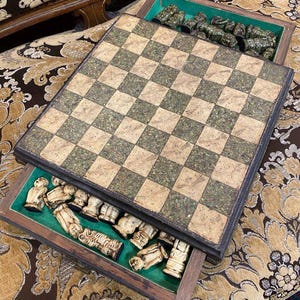 May include: A vintage chess set with a wooden board featuring a checkered pattern in beige and green. The set includes a drawer with green felt lining, holding chess pieces in off-white and green tones. The board is open, revealing the pieces.