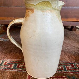 May include: A white ceramic pitcher with a brown and green glaze. The pitcher has a wide mouth and a handle.