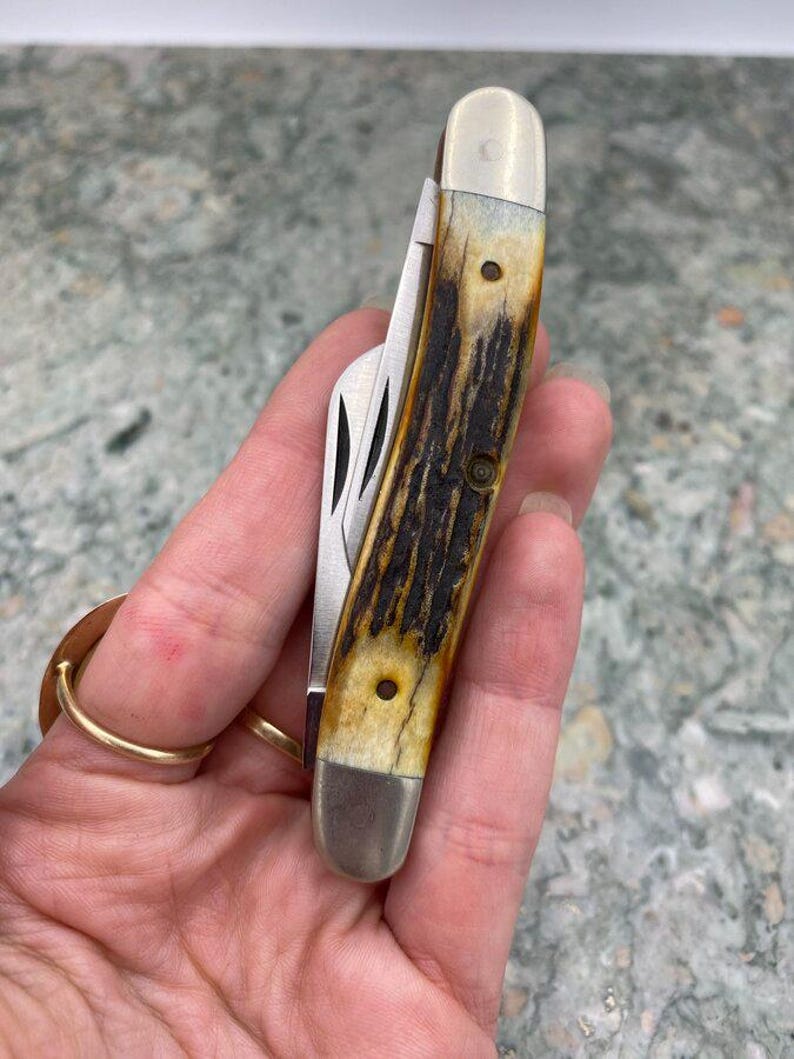 May include: A closed pocket knife with a handle displaying a brown and tan pattern, silver-coloured metal bolsters, and a stainless steel blade. The handle's textured design is visible.