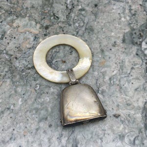 May include: A silver bell with a mother of pearl ring attached. The bell is tarnished and has a worn look.