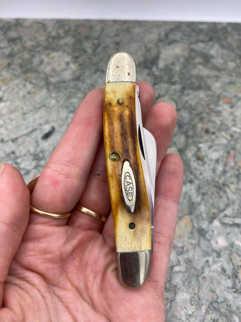 May include: A Case pocket knife with a brown and cream handle and a silver blade. The knife has a classic design with the "CASE" logo on the handle. The handle has brass rivets and a metal bolster.