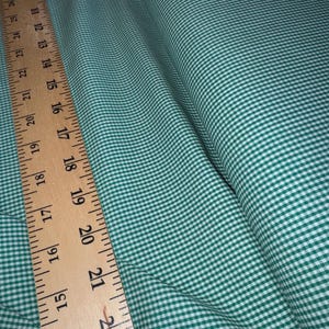 May include: A green and white gingham fabric featuring a small checkered pattern. A wooden ruler is placed along the edge of the fabric, showing measurements in inches, with the visible scale ranging from approximately 6 inches to 29 inches.