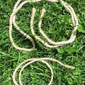 May include: Several loops of natural-colored rope are arranged on a bed of green grass. The rope appears to be made of a coarse, fibrous material, with a slightly twisted construction. The image is taken from a high angle, showing the rope against the green background.