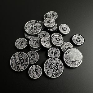Könnte beinhalten: Eine Sammlung silberfarbener Token mit einem geometrischen Design und der Zahl "5" darauf gedruckt. Die Token sind auf einer schwarzen Oberfläche verstreut.
