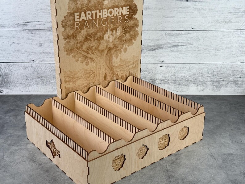 May include: A wooden organizer with the text "EARTHBORNE RANGERS" and a tree design. The organizer has multiple compartments and decorative cutouts. The lid is open, revealing the interior.