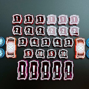 May include: A set of red, white, and black plastic game pieces with numbers 1 through 10, an X, and an exclamation point. The pieces are arranged in rows on a gray surface.