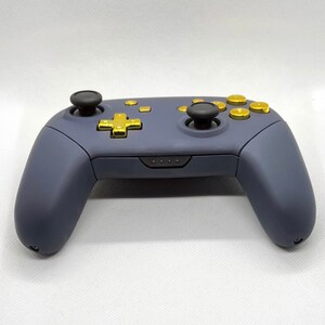 Op de afbeelding: Een donkerblauwe Nintendo Switch-controller met gouden knoppen. De controller heeft een standaard lay-out met twee analoge sticks, een D-pad en vier face buttons.