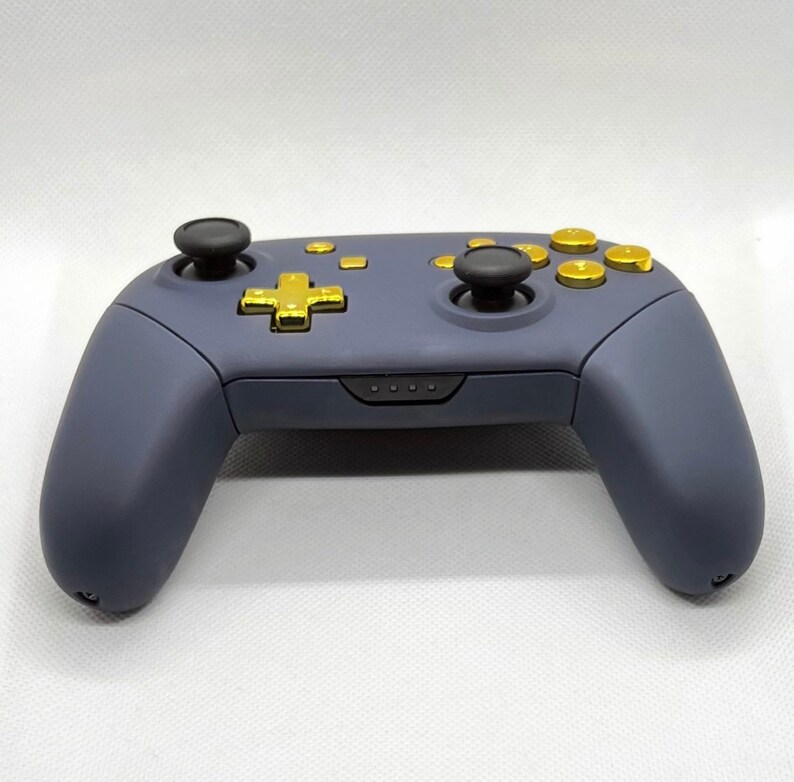 Op de afbeelding: Een donkerblauwe Nintendo Switch-controller met gouden knoppen. De controller heeft een standaard lay-out met twee analoge sticks, een D-pad en vier face buttons.
