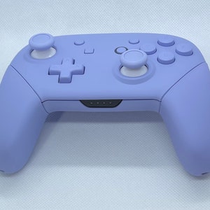 May include: A lavender purple Nintendo Switch controller with white buttons and a black faceplate.