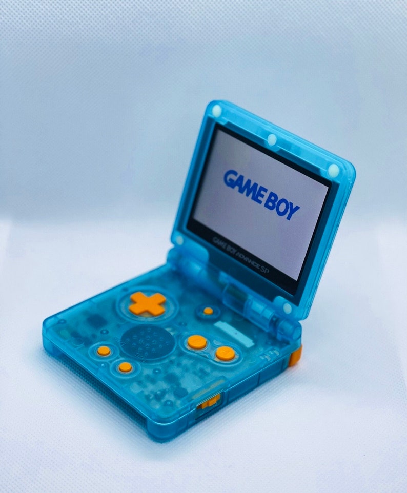 K&ouml;nnte beinhalten: Ein durchsichtiger blauer Game Boy Advance SP mit gelben Kn&ouml;pfen. Der Bildschirm ist ge&ouml;ffnet und zeigt das Game Boy-Logo.