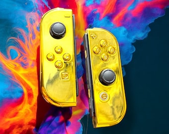 May include: Two gold-colored Nintendo Switch Joy-Con controllers with black buttons and a colorful background.