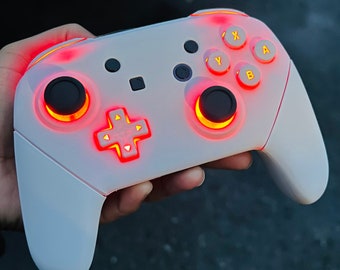 May include: A white Nintendo Switch controller with red and yellow illuminated buttons. The controller has a white, textured surface and a black faceplate.