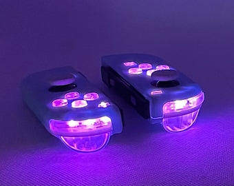 May include: Two white wireless game controllers with purple LED lights. The controllers have a variety of buttons and a joystick.