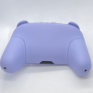 May include: A lavender purple video game controller with a black button panel.