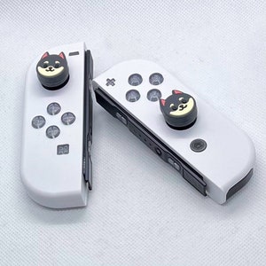 May include: Two white Nintendo Switch Joy-Con controllers with black and gray buttons. Each controller has a black and white dog face button cap.