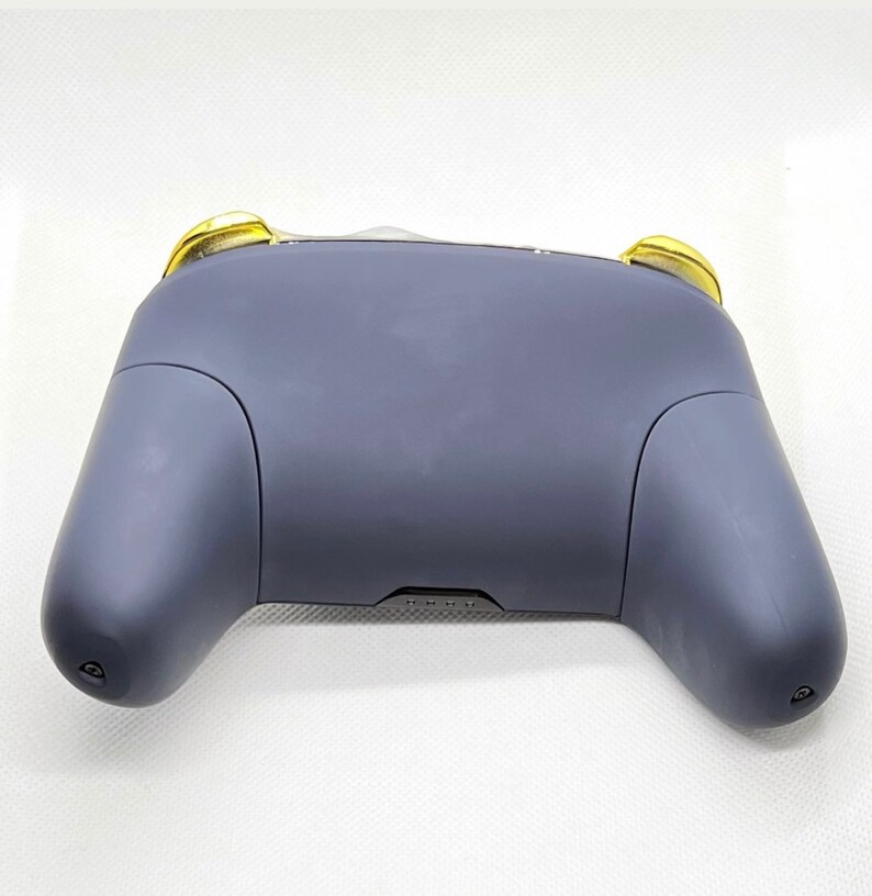 Op de afbeelding: Een donkergrijze videogamecontroller met gouden accenten aan de bovenkant. De controller heeft een textuur en is ontworpen voor gebruik met een gameconsole.