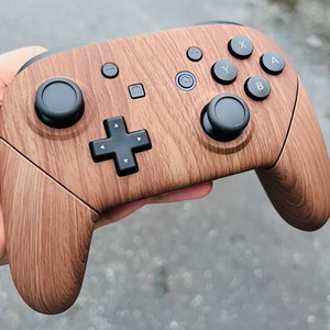 May include: A brown wooden Nintendo Switch controller with black buttons and a black d-pad. The controller has a wood grain pattern.