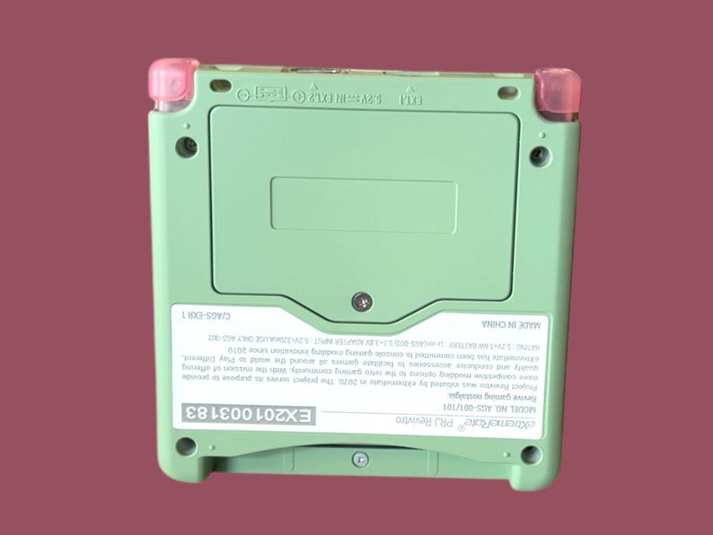 May include: A green Game Boy Advance SP with pink accents. The back of the device has a sticker with the text "eiktreme Rate PRJ Revivtro", "MODEL NO AGS-001/101", "Revive gaming nostalgia", "EX201003183", and a description of the project. The text "MADE IN CHINA" and "C/AGS-EXR 1" are also visible.