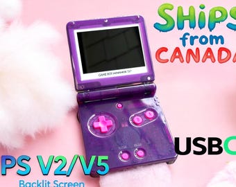 May include: A purple Game Boy Advance SP with a backlit screen. The screen is black and the console has pink buttons. The text "GAME BOY ADVANCE SP" is visible on the console. The text "IPS V2/V5 Backlit Screen" is visible in the bottom left corner of the image. The text "SHIPS from CANADA" is visible in the top right corner of the image. The text "USBC" is visible in the bottom right corner of the image.