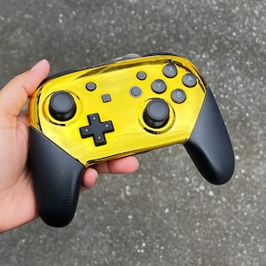 May include: A gold-coloured video game controller with black buttons and a textured grip. The controller has a black faceplate with the letters A, B, X, and Y on it.
