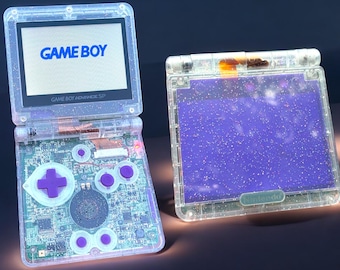 May include: A clear, glittery Game Boy Advance SP with a purple screen and the words "GAME BOY" and "GAME BOY ADVANCE SP" printed on the front.