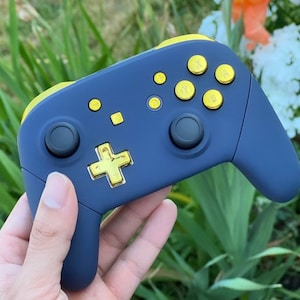 Op de afbeelding: Een donkerblauwe Nintendo Switch-controller met gouden knoppen. De controller heeft een textuur en een zwart D-pad.