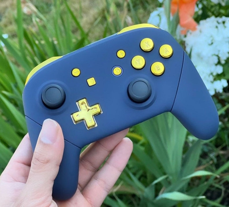 Op de afbeelding: Een donkerblauwe Nintendo Switch-controller met gouden knoppen. De controller heeft een textuur en een zwart D-pad.