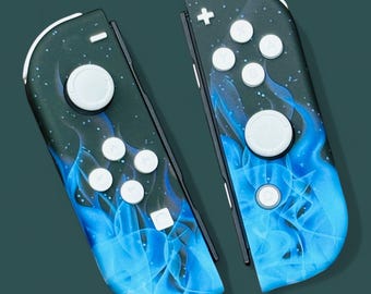 May include: A pair of blue and black Nintendo Switch Joy-Con controllers with a flame design. The controllers have white buttons and a plus sign on the top.