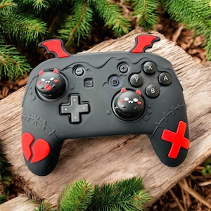 Può includere: Un controller di gioco nero e rosso dal design unico. Il controller presenta dettagli rossi, tra cui dettagli a forma di ali di pipistrello, un cuore spezzato e un pulsante a forma di croce. I cappucci del joystick hanno simpatici volti a tema diavolo.