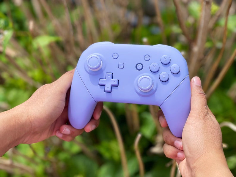 May include: A lavender purple Nintendo Switch controller with white buttons and joysticks.