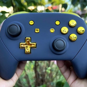 Op de afbeelding: Een donkerblauwe Nintendo Switch-controller met gouden knoppen en een gouden directionele pad.