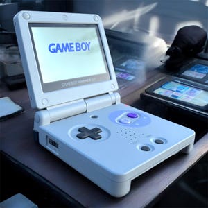 Op de afbeelding: Een lichtgrijze Game Boy Advance SP handheld gameconsole. Het scherm toont "GAME BOY" in blauw. De console heeft een kruisje, knoppen en de tekst "GAME BOY ADVANCE SP".