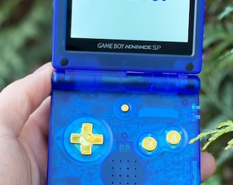 May include: A blue Game Boy Advance SP with gold buttons. The screen displays the text "GAME BOY" and "GAME BOY ADVANCE SP".