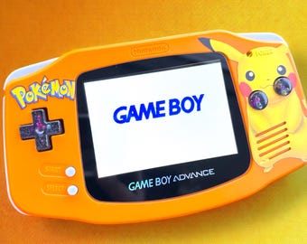 May include: Orange Game Boy Advance handheld game console with a Pikachu design. The screen displays "GAME BOY" in blue. The console features the "Pokémon" logo and a directional pad.