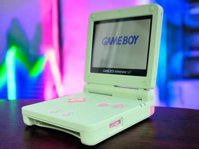 May include: A light green Game Boy Advance SP handheld gaming console with a white screen displaying the text "GAME BOY".