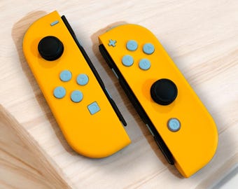 May include: A pair of yellow Nintendo Switch Joy-Con controllers. The left Joy-Con has a black analog stick and four gray buttons. The right Joy-Con has a black analog stick, four gray buttons, and a black button with a white circle in the center.