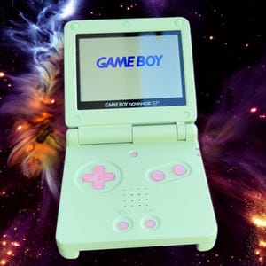 May include: A light green Game Boy Advance SP handheld gaming console with a pink button and a screen displaying the text "GAME BOY".
