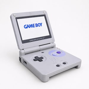 Op de afbeelding: Een lichtgrijze draagbare videogameconsole met een opklapbaar scherm waarop de blauwe tekst GAME BOY staat. Het apparaat is voorzien van een zwarte richtingspad, twee kleine zwarte knoppen met de labels SELECT en START en twee paarse knoppen.