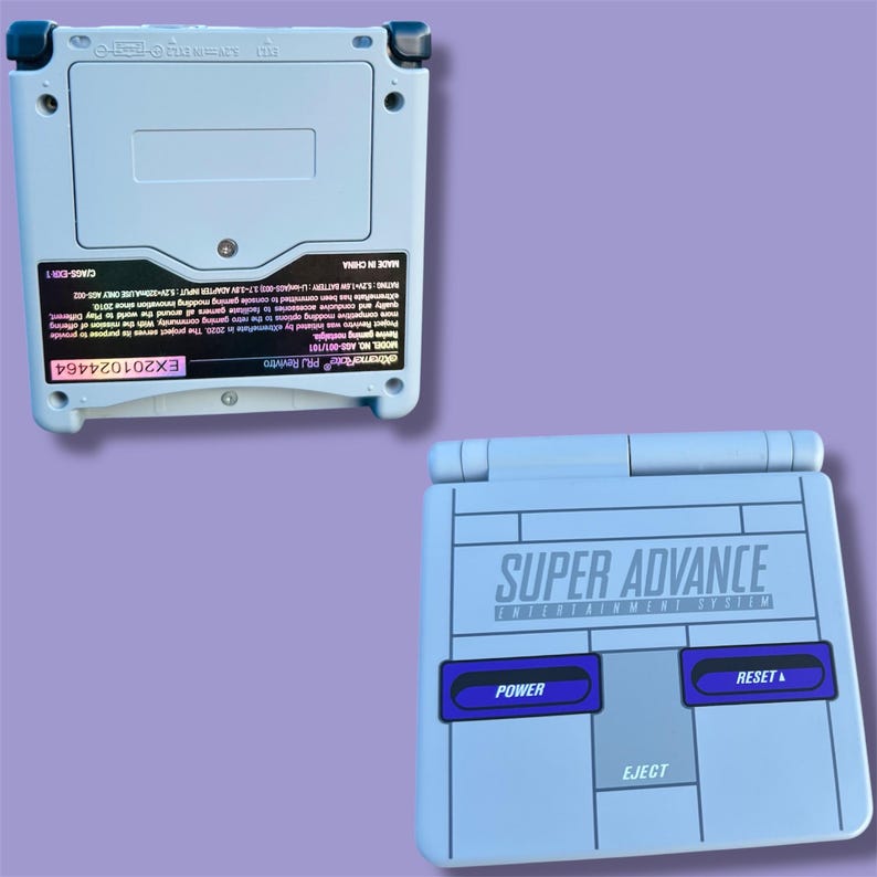 May include: Two light blue Super Advance handheld gaming consoles. One shows the back with a battery compartment and text. The other shows the front with the words "SUPER ADVANCE ENTERTAINMENT SYSTEM", "POWER", "RESET", and "EJECT" buttons.