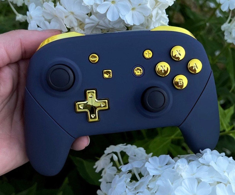 Op de afbeelding: Een marineblauwe Nintendo Switch-controller met gouden knoppen en face buttons. De controller heeft een gouden D-pad en een gouden rand rond de randen.