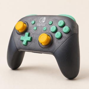 May include: A Nintendo Switch wireless controller featuring a translucent dark gray shell, two bright yellow analog sticks, and mint green buttons including a directional pad, A, B, X, Y, plus, minus, home, and capture buttons. The Nintendo Switch logo is printed in white on the center.