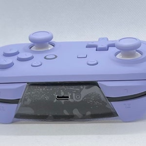 May include: A purple Nintendo Switch controller with white buttons and a USB-C port on the bottom.
