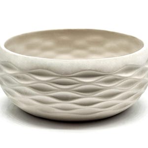 Może przedstawiać: Zestaw trzech ceramicznych kubków z nakrapianym, matowym wykończeniem. Kubki są w odcieniach kremu, jasnoszarym i ciemnoszarym. Każdy kubek ma prosty, minimalistyczny design i zaokrąglony uchwyt.
