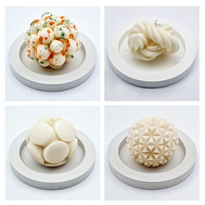May include: Four white candles on white circular bases. The candles are in different shapes: one is a cluster of small spheres, one is a swirl, one is a sphere with a geometric pattern, and one is a sphere with a smooth, rounded surface.