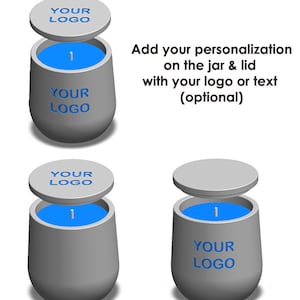 Könnte beinhalten: Zwei graue Kerzenbehälter mit blauem Wachs und Deckeln. Die Deckel tragen den Text "YOUR LOGO". Der Text "Fügen Sie Ihre Personalisierung auf dem Glas und dem Deckel mit Ihrem Logo oder Text hinzu (optional)" wird über den Behältern angezeigt.