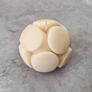 May include: A round, off-white candle with a textured surface. The candle is made up of multiple circles that are joined together to form a sphere.