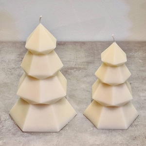 May include: Two white geometric candle sculptures shaped like Christmas trees. The larger candle has five tiers and the smaller candle has four tiers.
