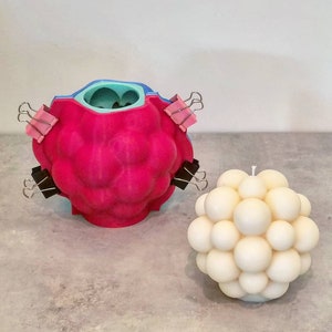 May include: A pink silicone mold with a blue interior, held together with binder clips, and a white bubble candle.